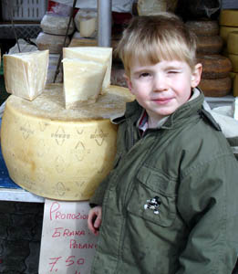 Joshua squints into the sunlights at a market in Valledoria.  The cheese next to him is locally made parmesan